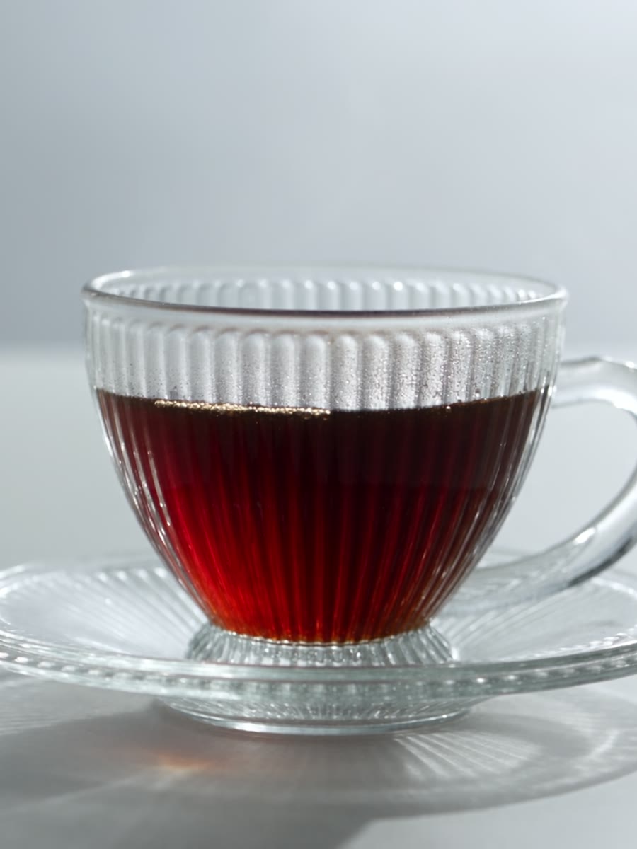 Xícara de vidro canelado com café coado sobre pires, centralizada em fundo claro.