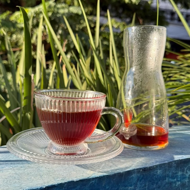 Xícara de vidro canelado com café coado e decanter ao lado, na varanda.