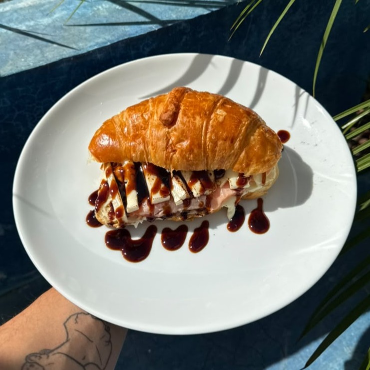 Croissant Dope aberto, com queijo canastra e molho tarê, servido no prato.