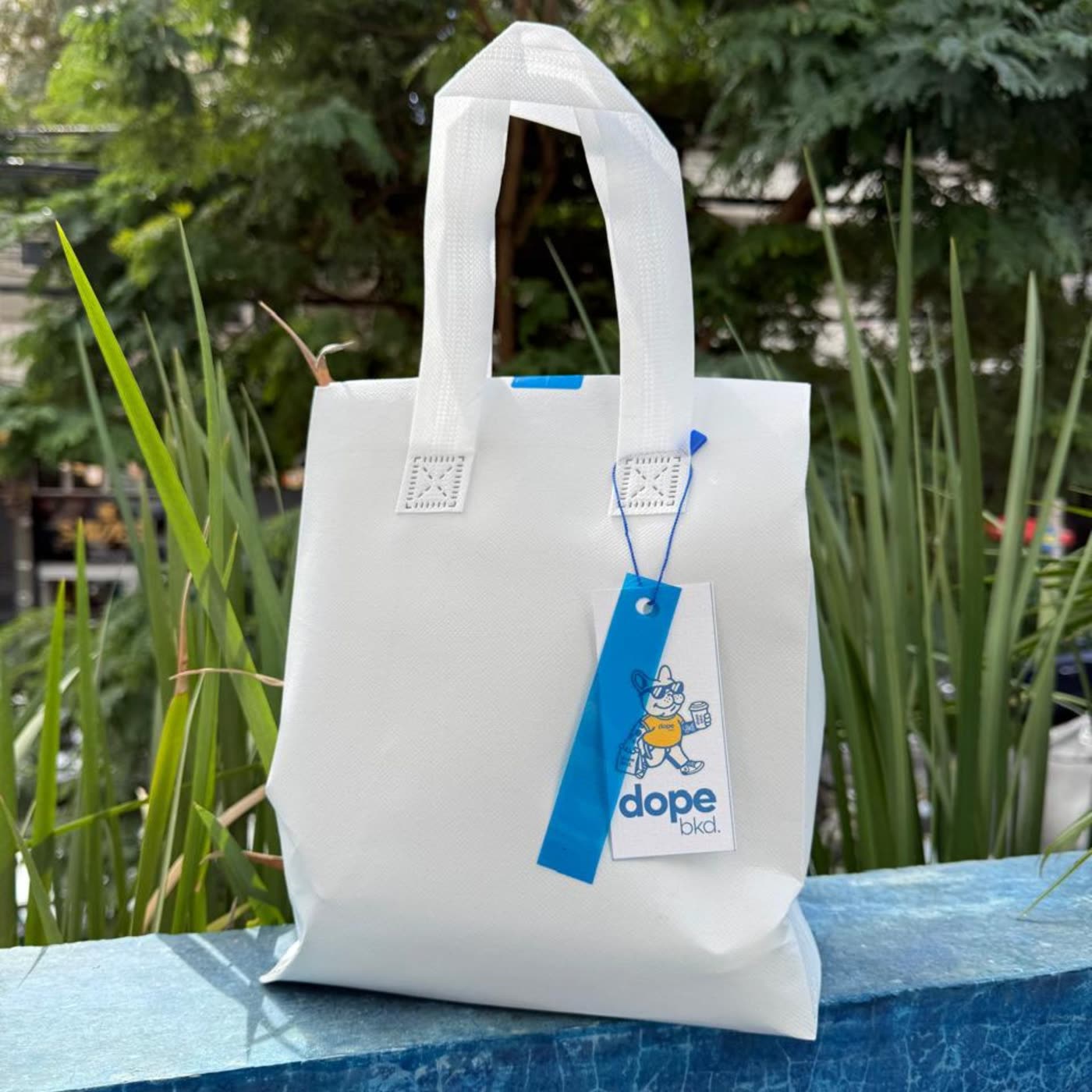 Sacola branca de entrega da Dope Baked com tag azul da marca.